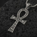 Load image into Gallery viewer, Oxidized ankh cross pendant necklace on textured volcanic rock, close-up studio shot highlighting the ancient Egyptian key of life symbol, hieroglyphic details, and antique silver contrast.