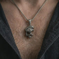 Load image into Gallery viewer, Oxidized cracked skull pendant necklace worn on the chest, close-up lifestyle jewelry photo showing the gothic skull charm on a spiga chain with dark clothing.