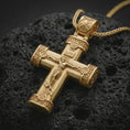 Load image into Gallery viewer, Gold plated crucifix cross pendant necklace on textured volcanic rock, premium close-up studio composition emphasizing the sacred cross shape, religious details, and bold Christian medallion design.