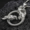 Load image into Gallery viewer, Polished silver Hugin and Munin ravens pendant necklace on textured volcanic rock, centered macro jewelry photo with detailed Norse bird relief and bright silver highlights.