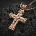 Load image into Gallery viewer, Rose gold plated crucifix cross pendant necklace on textured volcanic rock, detailed macro product shot with soft warm reflections and devotional Christian symbolism.