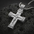 Load image into Gallery viewer, Polished silver crucifix cross pendant necklace on textured volcanic rock, centered macro jewelry photo with detailed Christ relief, engraved accents, and bright silver highlights.