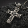 Load image into Gallery viewer, Oxidized crucifix cross pendant necklace on textured volcanic rock, close-up studio shot highlighting the Jesus figure, INRI plaque, ornate barrel ends, and antique silver contrast.
