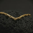 Load image into Gallery viewer, Gold plated Greek key chain laid across textured volcanic rock, emphasizing the classical meander motif and structured link-by-link construction.