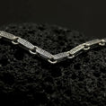 Load image into Gallery viewer, Oxidized sterling silver Greek key chain shown across black volcanic rock, highlighting the antique meander pattern engraved into each rectangular link.