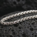 Load image into Gallery viewer, Polished silver box chain necklace on volcanic stone, highlighting the clean segmented link pattern and reflective sterling finish.