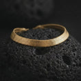 Load image into Gallery viewer, Gold plated flat herringbone bracelet on volcanic rock, highlighting the smooth wrist-hugging shape and structured chevron design.