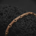 Load image into Gallery viewer, Rose gold plated meander bracelet displayed on rugged volcanic rock in a refined dark studio macro photograph.