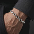 Load image into Gallery viewer, Polished silver Greek meander chain bracelet worn on a man’s wrist, with the alternating round and rectangular links clearly visible in a detailed lifestyle photograph.