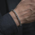 Load image into Gallery viewer, Oxidized Greek key bracelet worn on a man’s wrist, displaying the dark recessed meander engravings and elongated silver links in a masculine close-up lifestyle shot.