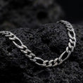 Load image into Gallery viewer, A 7mm Figaro chain necklace with an oxidized finish rests on dark volcanic rock, showing the classic three short links and one elongated oval link in a macro studio close-up.