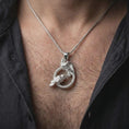 Load image into Gallery viewer, Polished silver Hugin and Munin ravens pendant necklace worn on the chest, masculine lifestyle shot highlighting the bright silver finish, sculpted feathers, and braided circular frame.