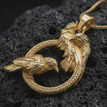 Load image into Gallery viewer, Gold plated Hugin and Munin ravens pendant necklace on textured volcanic rock, premium close-up studio composition emphasizing the Viking raven pair, braided ring, and mythological amulet design.