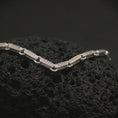 Load image into Gallery viewer, Polished silver Greek key chain necklace displayed on dark volcanic stone, with bright edges and detailed repeating geometric links clearly visible.