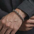 Load image into Gallery viewer, Oxidized sterling silver ornamental bracelet worn on a male wrist, showing its textured circle-link design and refined vintage character.