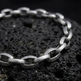 Load image into Gallery viewer, Sterling silver Greek key bracelet with an oxidized finish arranged on dark volcanic rock, showing engraved circular meander links and smooth rectangular connectors in a macro studio close-up.