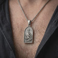 Load image into Gallery viewer, An oxidized Jesus carrying the cross pendant is worn on a man’s neck, displaying the dark recessed relief, INRI inscription, and detailed kneeling figure in a masculine lifestyle close-up.