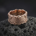 Load image into Gallery viewer, The rose gold plated fantasy claw ring is arranged on black volcanic rock, emphasizing its wide profile, layered scale texture, and mythical dragon-inspired construction in a refined macro image.
