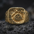 Load image into Gallery viewer, A gold plated Norse rune ring rests on rugged volcanic rock, featuring a raised Valknut symbol surrounded by ancient-style lettering and a small skull detail in a luxury macro studio close-up.