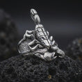 Load image into Gallery viewer, The polished silver scorpion ring is displayed on textured black volcanic rock, highlighting the dimensional arachnid body, pointed claws, raised tail, and sculpted side details in a premium macro photograph.