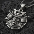Load image into Gallery viewer, A detailed samurai warrior pendant with an oxidized finish rests on black volcanic rock, showing the kabuto helmet, armored face mask, crossed swords, and circular rope border in a macro studio close-up.