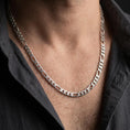 Load image into Gallery viewer, The polished silver 7mm Figaro necklace is worn on a man’s chest, displaying the alternating short curb links and elongated oval links in a refined lifestyle photograph.
