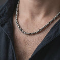 Load image into Gallery viewer, A ridged barrel chain necklace with an oxidized finish is worn on a man’s neck, displaying dark recessed details, rounded connectors, and a bold masculine silhouette in a close-up lifestyle shot.