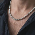 Load image into Gallery viewer, The polished silver cylinder link necklace is worn on a man’s chest, showing the repeating barrel sections and articulated chain movement in a premium lifestyle photograph.