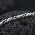 Load image into Gallery viewer, The polished silver barrel chain necklace is displayed on textured black volcanic rock, highlighting the raised ridges, smooth link openings, and articulated sterling silver construction in a premium macro photograph.