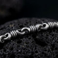 Load image into Gallery viewer, A ridged barrel chain necklace with an oxidized finish rests on dark volcanic rock, showing rounded connector links and sculpted cylinder sections in a macro studio close-up.