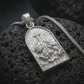 Load image into Gallery viewer, The polished silver Jesus cross pendant is displayed on textured volcanic rock, highlighting the arched medallion, raised INRI lettering, flowing garments, and dimensional Christian relief in a premium macro photograph.