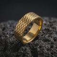 Load image into Gallery viewer, A gold plated crosshatch ring rests on rugged volcanic rock, featuring a repeating diagonal lattice pattern across its wide unisex band in a luxury macro studio close-up.