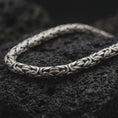 Load image into Gallery viewer, A 6mm Byzantine chain necklace with an oxidized finish rests on dark volcanic rock, showing its rounded interlocking links and woven sterling silver structure in a macro studio close-up.