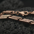 Load image into Gallery viewer, The rose gold plated scroll link necklace is arranged on black volcanic rock, emphasizing its engraved bar links, flexible chain structure, and refined ornamental detailing in a detailed macro image.