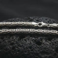 Load image into Gallery viewer, The polished silver 4mm square Byzantine chain necklace is displayed on textured black volcanic rock, emphasizing its intricate link pattern and refined geometric silhouette in a premium macro photograph.