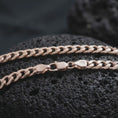 Load image into Gallery viewer, The rose gold plated Cuban chain necklace is arranged on black volcanic rock, emphasizing its 5mm curb link construction, flexible structure, and timeless polished surface in a detailed macro image.