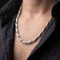 Load image into Gallery viewer, The polished silver Greek meander chain is worn on a man’s chest, showing the repeating link pattern and bold historical styling in a premium lifestyle photograph.