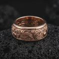 Load image into Gallery viewer, The rose gold plated carp wave ring is arranged on black volcanic rock, emphasizing the flowing water relief, raised fish elements, and refined unisex spinning band design in a detailed macro image.