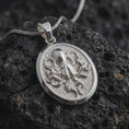 Load image into Gallery viewer, The polished silver octopus necklace is displayed on textured black volcanic rock, highlighting the dimensional sea creature, flowing tentacles, smooth circular frame, and detailed marine relief in a premium macro photograph.