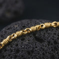 Load image into Gallery viewer, A gold plated ridged barrel necklace lies across rugged volcanic rock, featuring repeating cylinder links, rounded connectors, and a bold masculine chain profile in a luxury macro studio close-up.