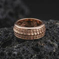 Load image into Gallery viewer, A rose gold plated reptile spinner ring is arranged on dark volcanic rock, featuring a detailed lizard scale pattern, elegant rotating band structure, and warm metallic finish in a close-up product photograph.