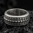 Load image into Gallery viewer, An oxidized sterling silver lizard scale spinner ring rests on dark volcanic rock, highlighting the rotating reptile texture, rugged pattern, and bold band design in a dramatic macro close-up.