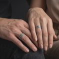 Load image into Gallery viewer, An oxidized Aztec spinner ring is worn on a finger, displaying the dark recessed symbols, wide sterling silver band, and tactile fidget ring design in a close-up lifestyle shot.