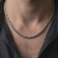 Load image into Gallery viewer, An oxidized 4mm square Byzantine chain necklace is worn on a man’s neck, showing its darkened recessed details and structured sterling silver weave in a close-up lifestyle shot.
