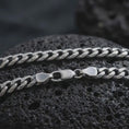 Load image into Gallery viewer, A 5mm Cuban chain necklace with an oxidized finish rests on dark volcanic rock, showing its flattened curb links and classic sterling silver structure in a macro studio close-up.