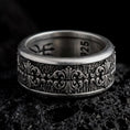Load image into Gallery viewer, An oxidized sterling silver Baroque fleur-de-lis spinner ring rests on dark volcanic rock, showing raised scrollwork, ornate floral motifs, and a textured recessed wide band in a macro studio close-up.