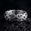 Load image into Gallery viewer, An oxidized sterling silver Byzantine chain band ring rests on dark volcanic rock, showing sculpted interlocking links, woven chain texture, and a substantial wide band in a macro studio close-up.