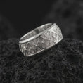 Load image into Gallery viewer, The polished silver flower wedding band is displayed on textured black volcanic rock, highlighting the repeating floral pattern, smooth rounded edges, and wide spinner ring profile in a premium macro photograph.