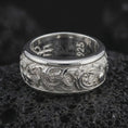 Load image into Gallery viewer, The polished silver carp and wave wedding band is displayed on textured black volcanic rock, highlighting the sculpted fish motifs, ornamental water lines, and wide spinner ring profile in a premium macro photograph.