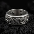 Load image into Gallery viewer, An oxidized sterling silver koi fish spinner ring rests on dark volcanic rock, showing raised carp details, flowing wave patterns, and a dark recessed band background in a macro studio close-up.